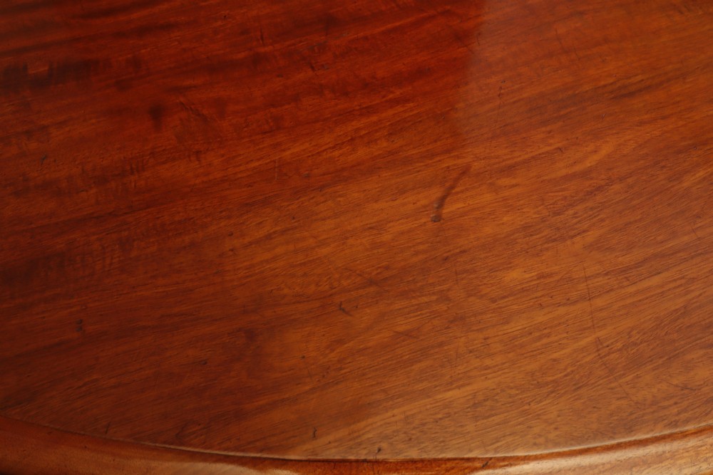 A circular Victorian flame mahogany dining table resting on a turned pedestal with four carved scroll legs. View VI