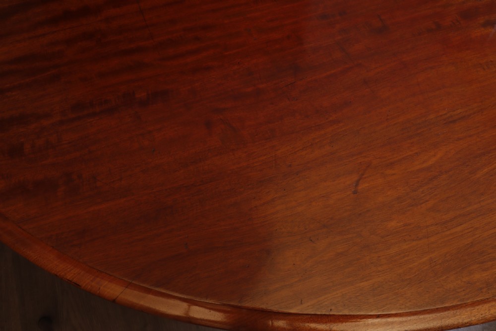 A circular Victorian flame mahogany dining table resting on a turned pedestal with four carved scroll legs. View IX
