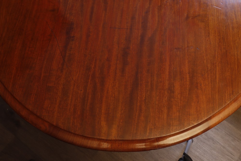A circular Victorian flame mahogany dining table resting on a turned pedestal with four carved scroll legs. View X