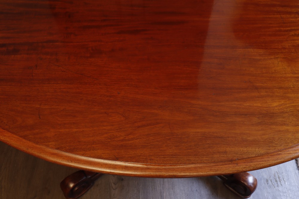 A circular Victorian flame mahogany dining table resting on a turned pedestal with four carved scroll legs. View XI