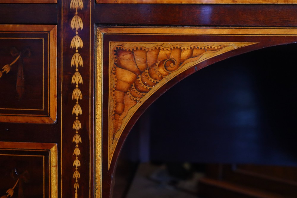 A mahogany writing desk featuring floral marquetry swags, seven drawers with brass handles, a central arch kneehole, and tapered legs on brass castors. View II