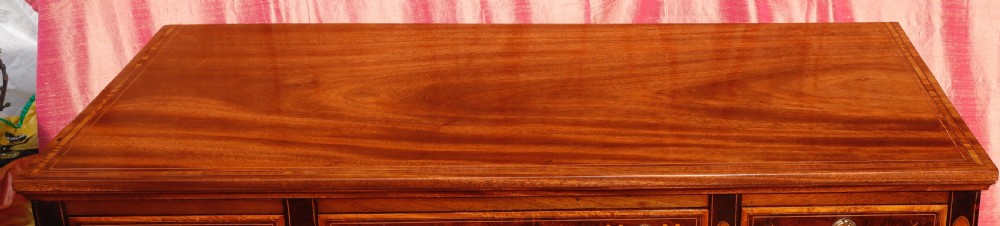 A mahogany writing desk featuring floral marquetry swags, seven drawers with brass handles, a central arch kneehole, and tapered legs on brass castors. View VI