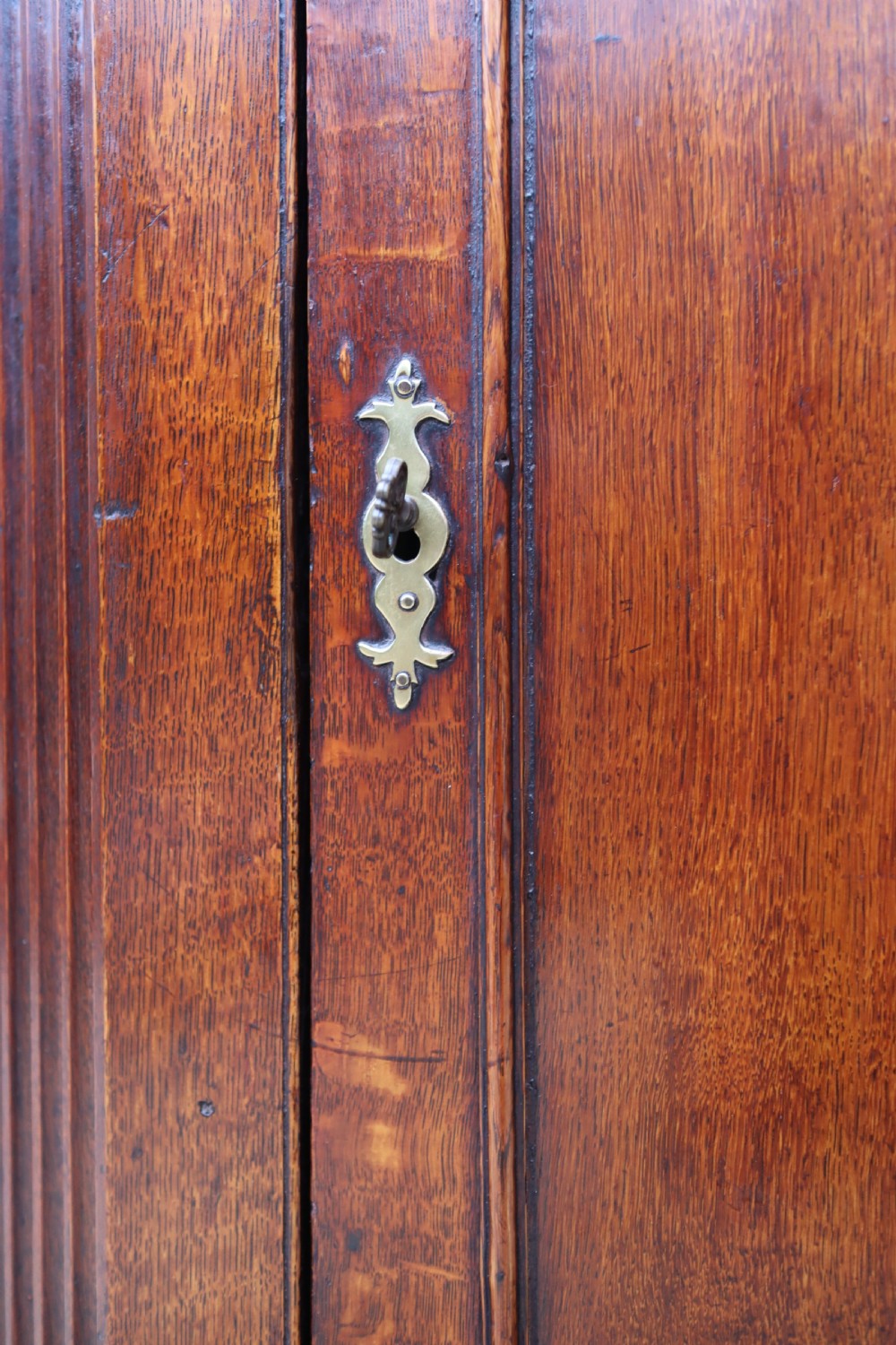 An antique oak corner cupboard featuring a single door with central oval starburst inlay, fluted pilasters, brass H-hinges, and a dentil moulding cornice. View III