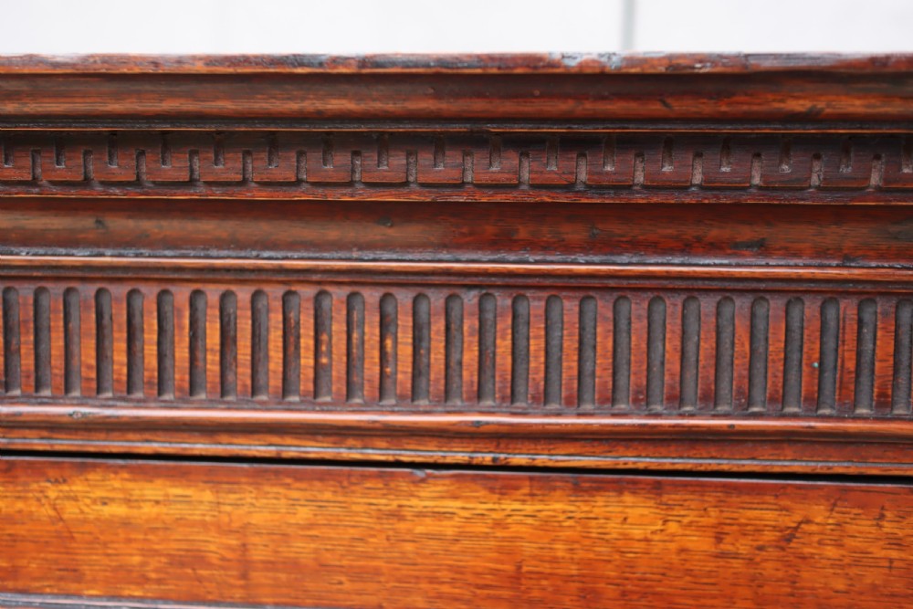 An antique oak corner cupboard featuring a single door with central oval starburst inlay, fluted pilasters, brass H-hinges, and a dentil moulding cornice. View V