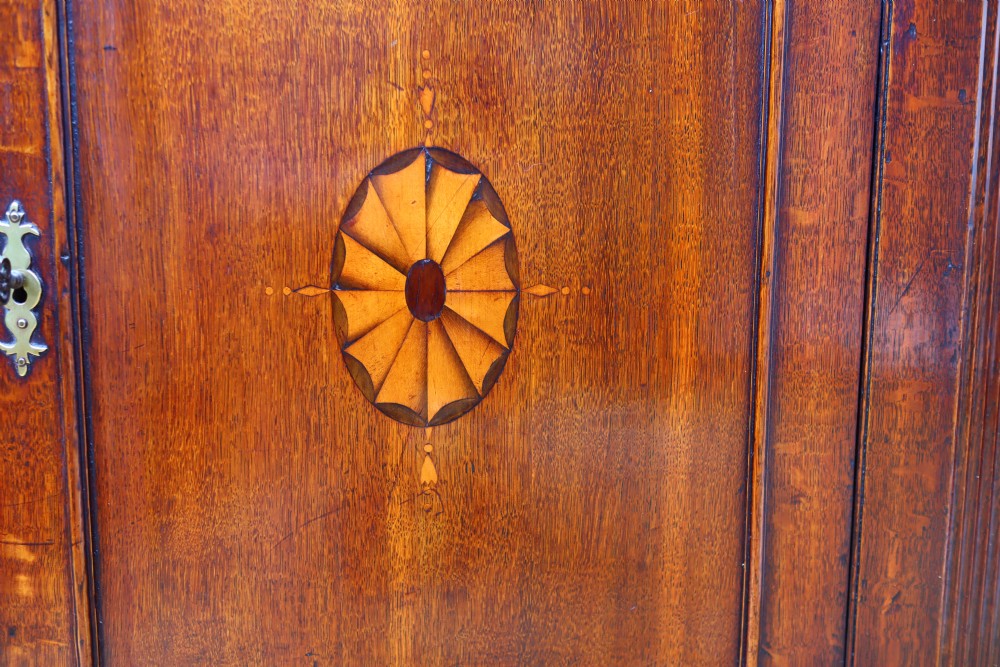 An antique oak corner cupboard featuring a single door with central oval starburst inlay, fluted pilasters, brass H-hinges, and a dentil moulding cornice. View VII