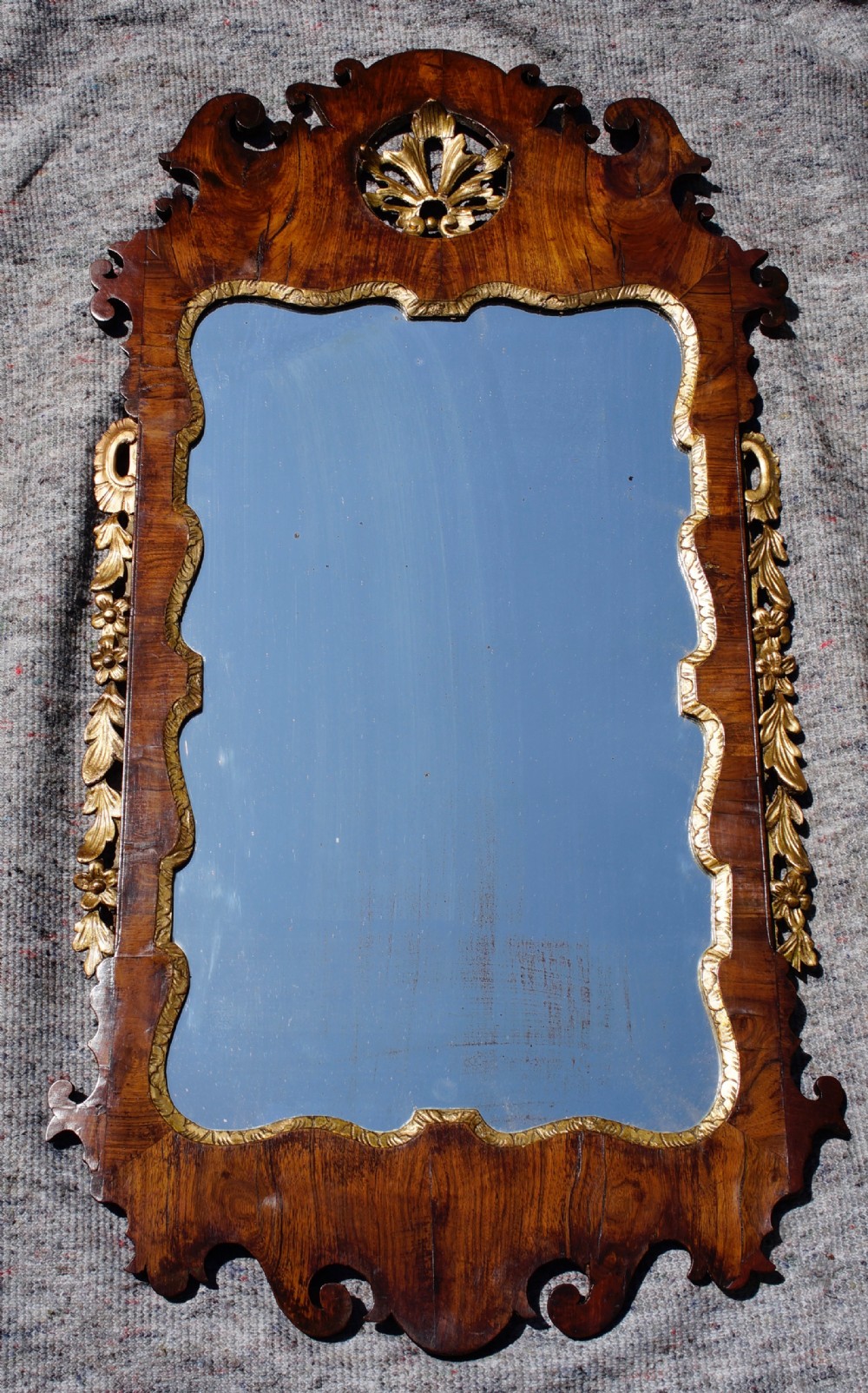 A George II walnut wall mirror featuring a shaped fretwork frame, parcel-gilded mouldings, and a carved crest motif.