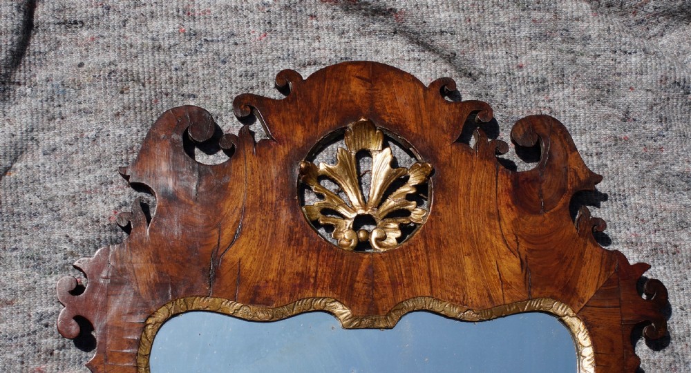 A George II walnut wall mirror featuring a shaped fretwork frame, parcel-gilded mouldings, and a carved crest motif. View V
