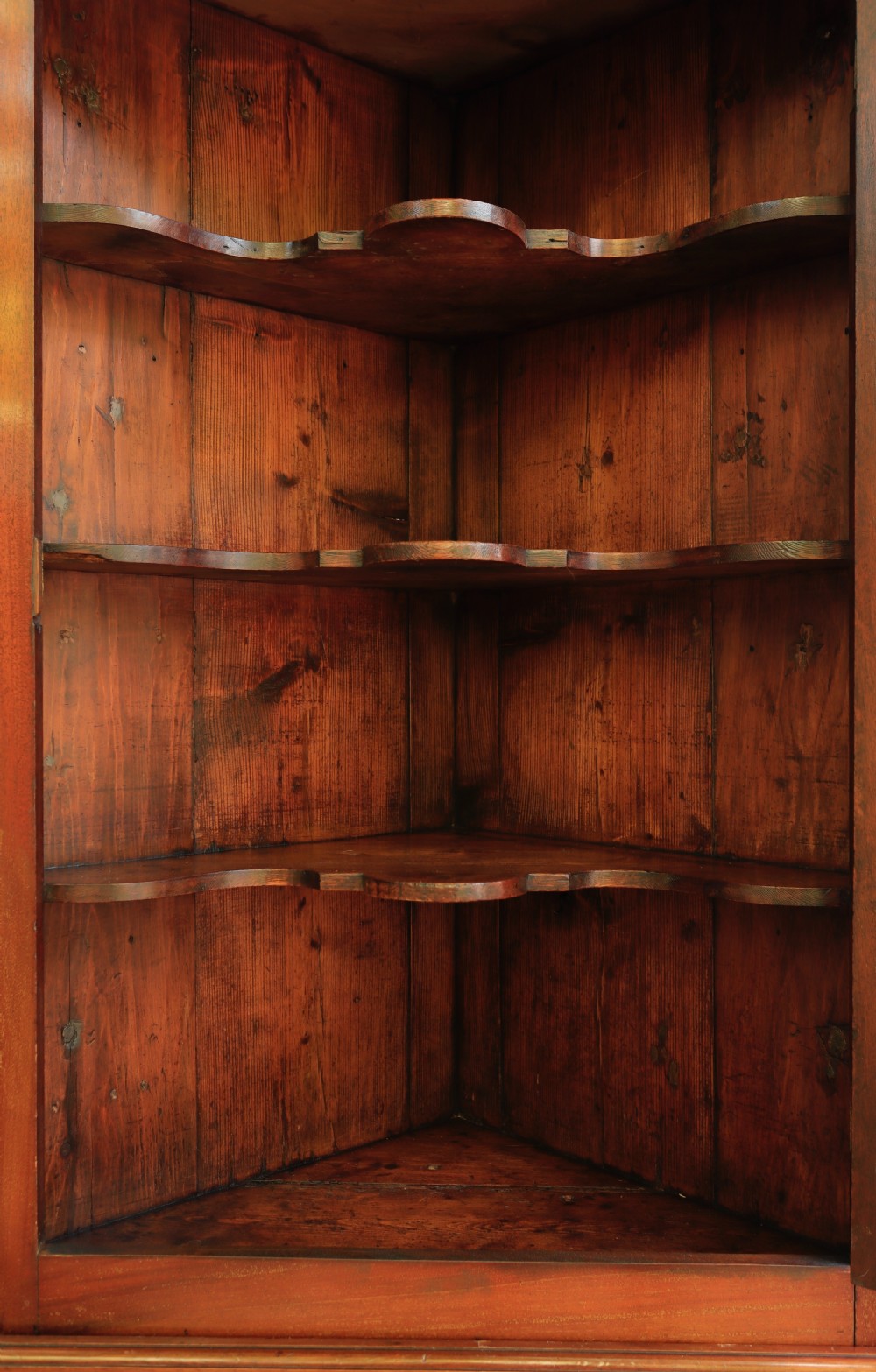 A tall, free-standing antique mahogany corner cupboard featuring two stacked panel doors decorated with carved corner details and top dentil moulding. View III