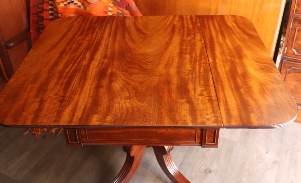 A mahogany pedestal dining table featuring drop-leaf sides, turned central column, four reeded splayed legs, and brass castors. View II