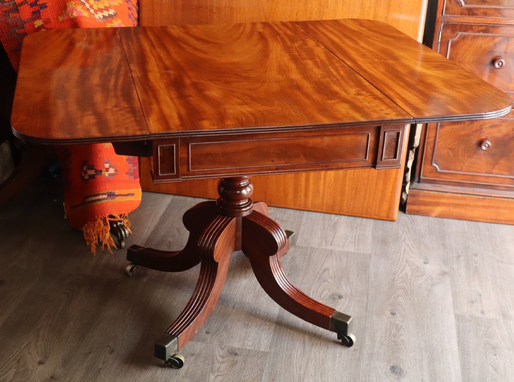 A mahogany pedestal dining table featuring drop-leaf sides, turned central column, four reeded splayed legs, and brass castors. View III