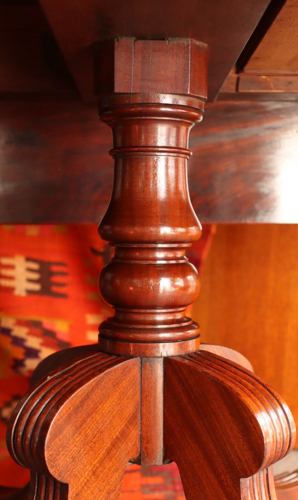 A mahogany pedestal dining table featuring drop-leaf sides, turned central column, four reeded splayed legs, and brass castors. View XIV