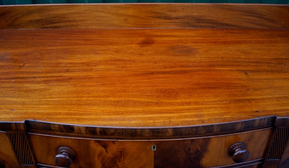 An antique Regency flame mahogany sideboard featuring spiral-reeded legs, turned wooden drawer knobs, an arched central apron, and a low rear gallery. View VI