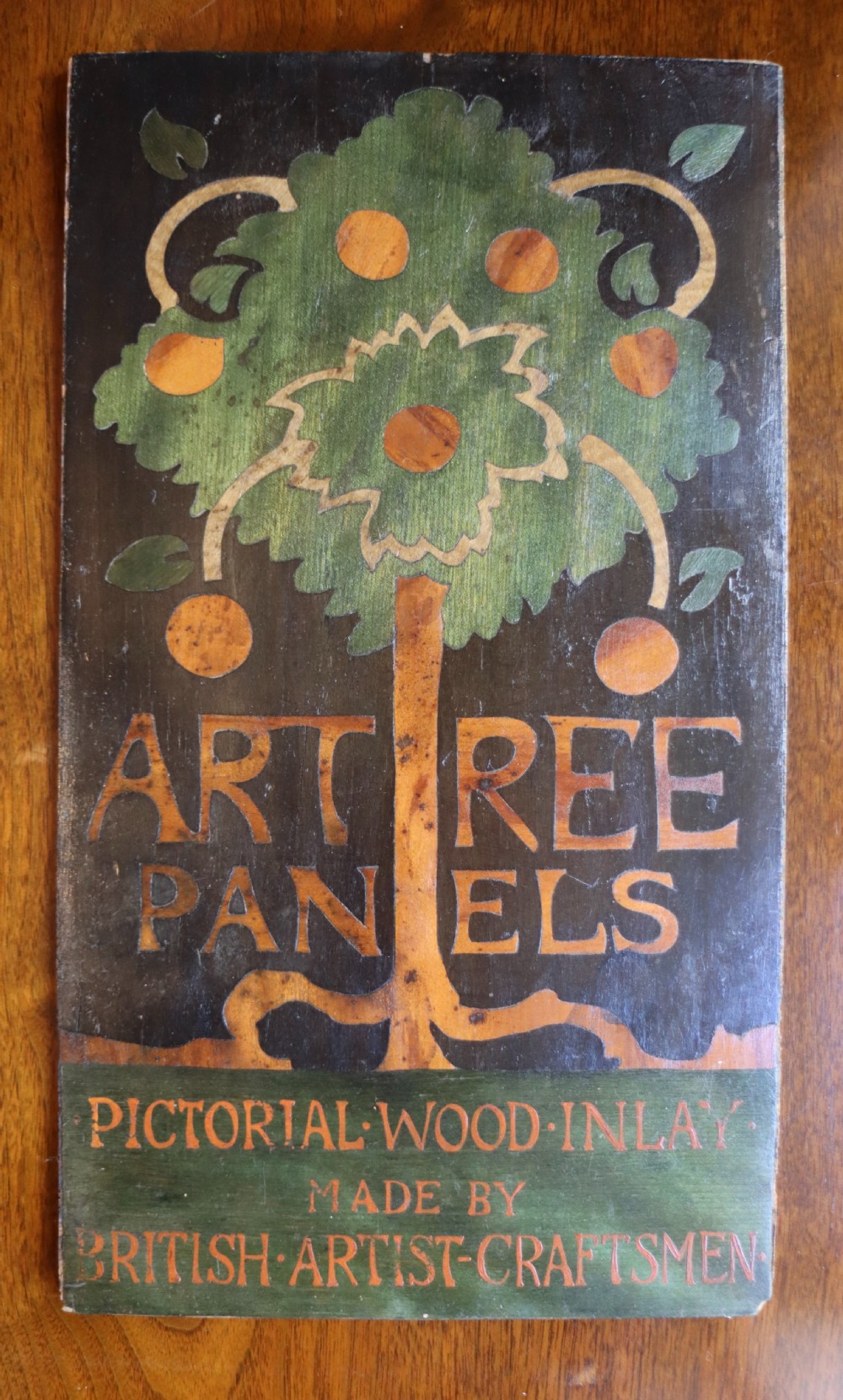 A rectangular wooden marquetry wall panel depicting a stylised green tree with fruit and inlaid lettering reading Art Tree Panels.