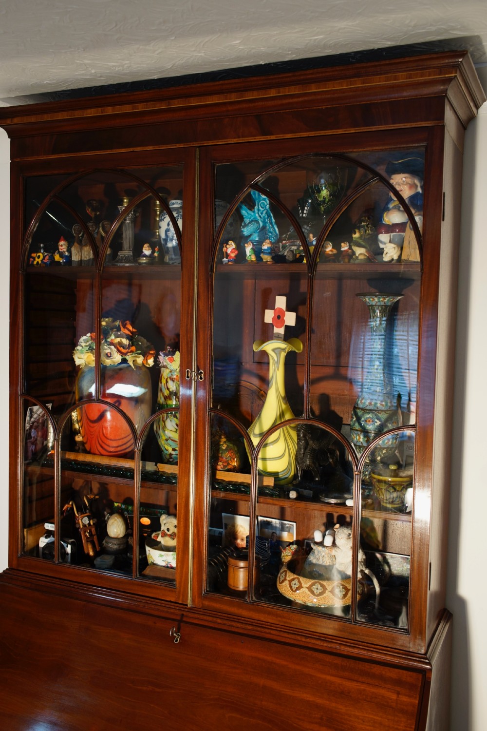 An antique mahogany bureau bookcase with astragal glazed doors above a slant-front writing desk and three lower drawers with brass handles. View II