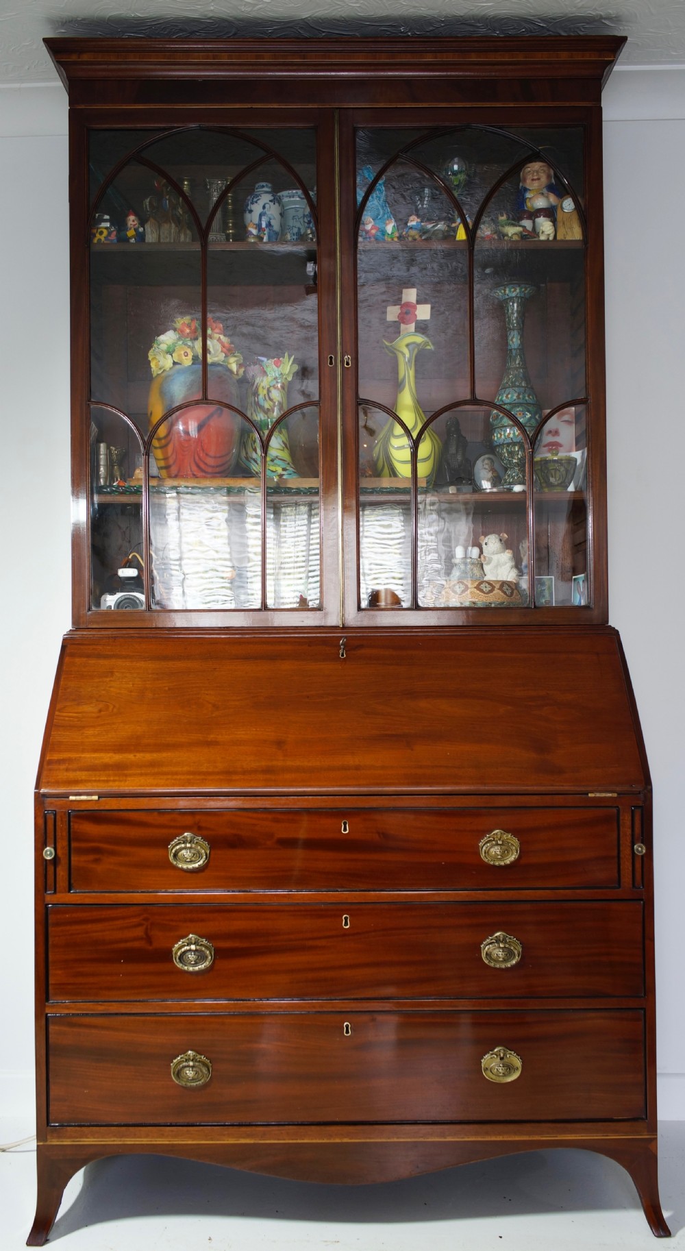 An antique mahogany bureau bookcase with astragal glazed doors above a slant-front writing desk and three lower drawers with brass handles. View V