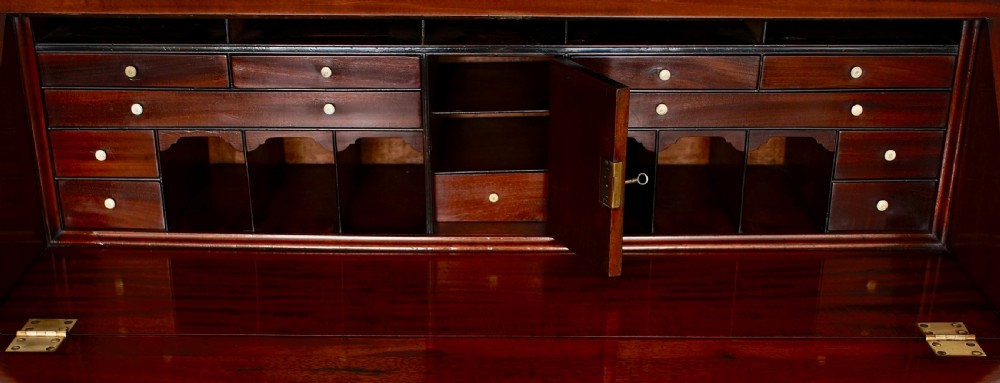 An antique mahogany bureau bookcase with astragal glazed doors above a slant-front writing desk and three lower drawers with brass handles. View VI