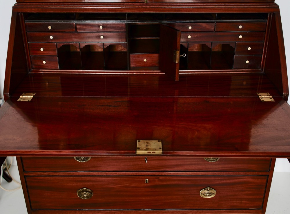 An antique mahogany bureau bookcase with astragal glazed doors above a slant-front writing desk and three lower drawers with brass handles. View VII