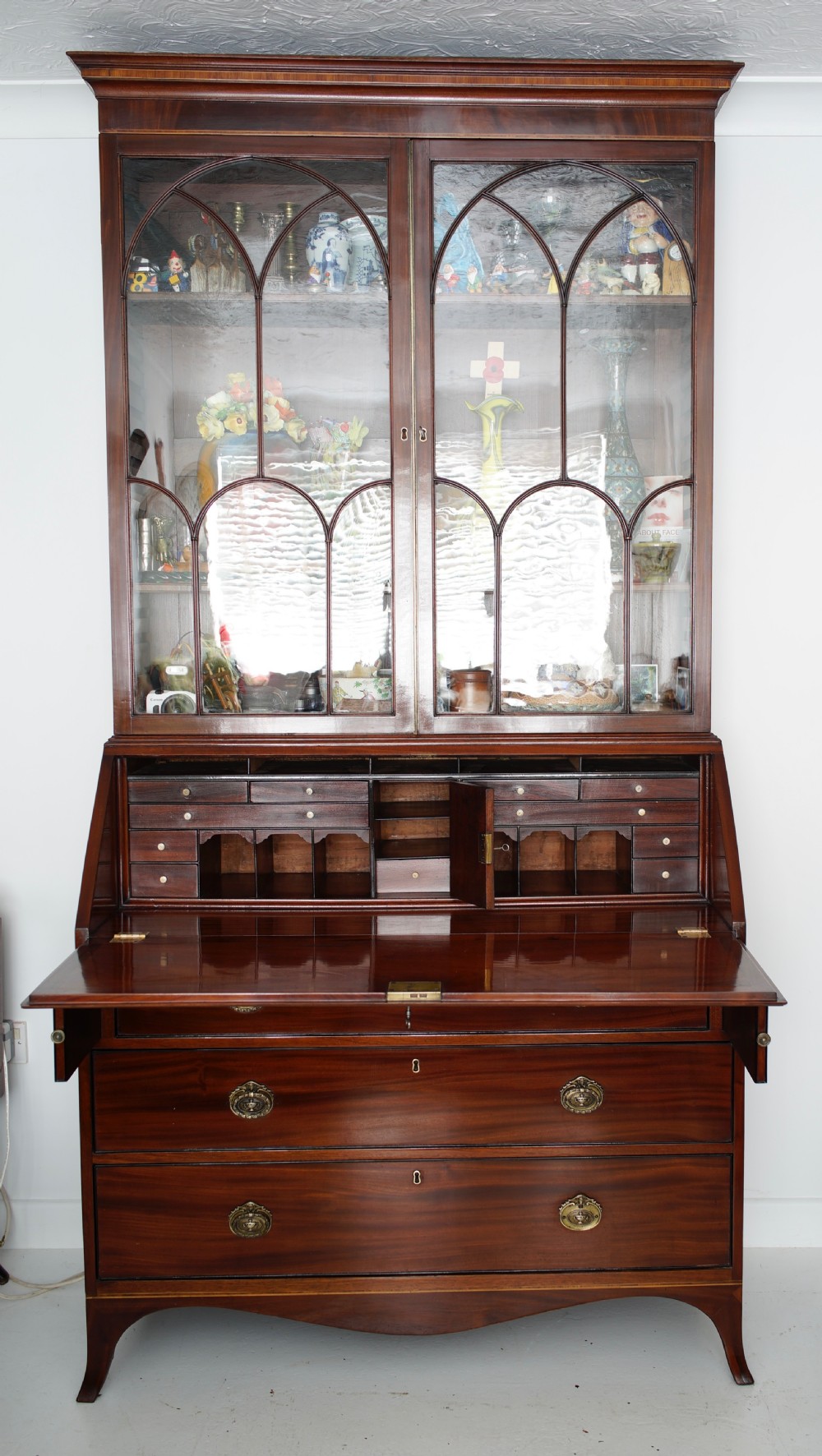 An antique mahogany bureau bookcase with astragal glazed doors above a slant-front writing desk and three lower drawers with brass handles. View VIII