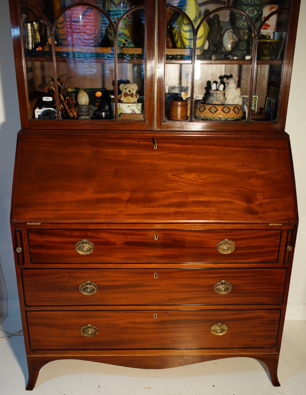 An antique mahogany bureau bookcase with astragal glazed doors above a slant-front writing desk and three lower drawers with brass handles. View IX