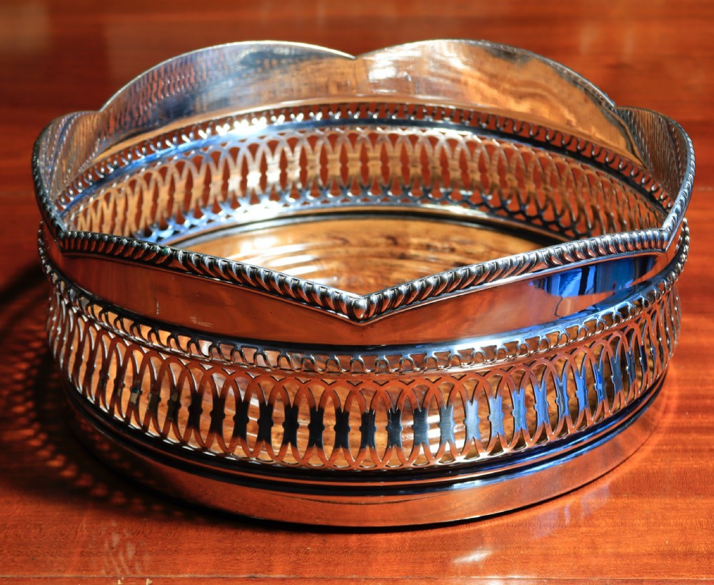 A silver-plated bottle coaster featuring a pierced gallery, a scalloped rim with rope-twist edging, and a turned wooden base.