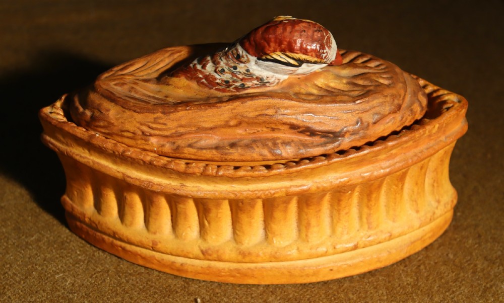 An oval terracotta game pie dish featuring a fluted base and a woven pastry lid topped with a painted bird head finial. View II