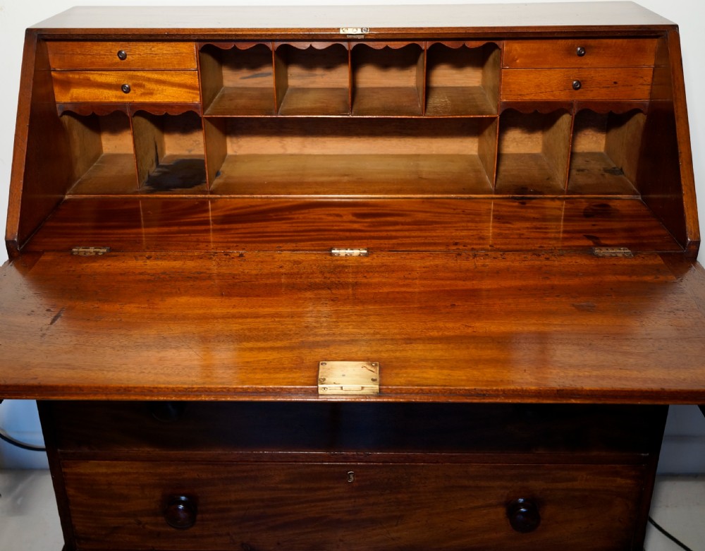 An antique warm brown mahogany bureau featuring a slant-front lid above three long drawers with turned wooden handles, set on turned feet. View IV