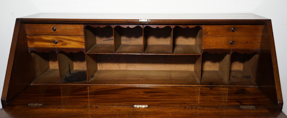 An antique warm brown mahogany bureau featuring a slant-front lid above three long drawers with turned wooden handles, set on turned feet. View II