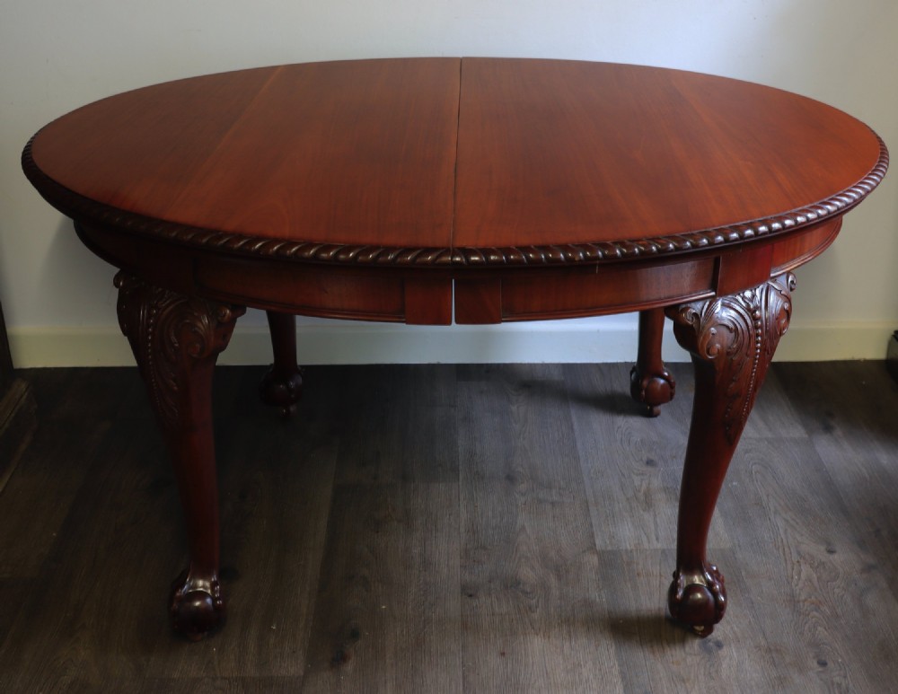 A circular mahogany antique extending dining table featuring carved cabriole legs with ball and claw feet and a rope-carved rim edge.