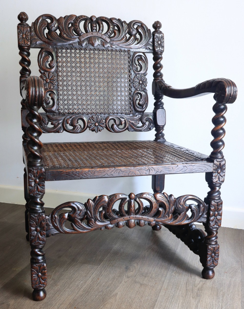 A dark carved oak armchair featuring barley twist supports, a woven cane back panel, and intricate foliate crown carving on the cresting rail.