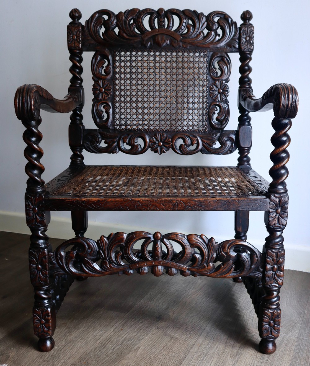 A dark carved oak armchair featuring barley twist supports, a woven cane back panel, and intricate foliate crown carving on the cresting rail. View II