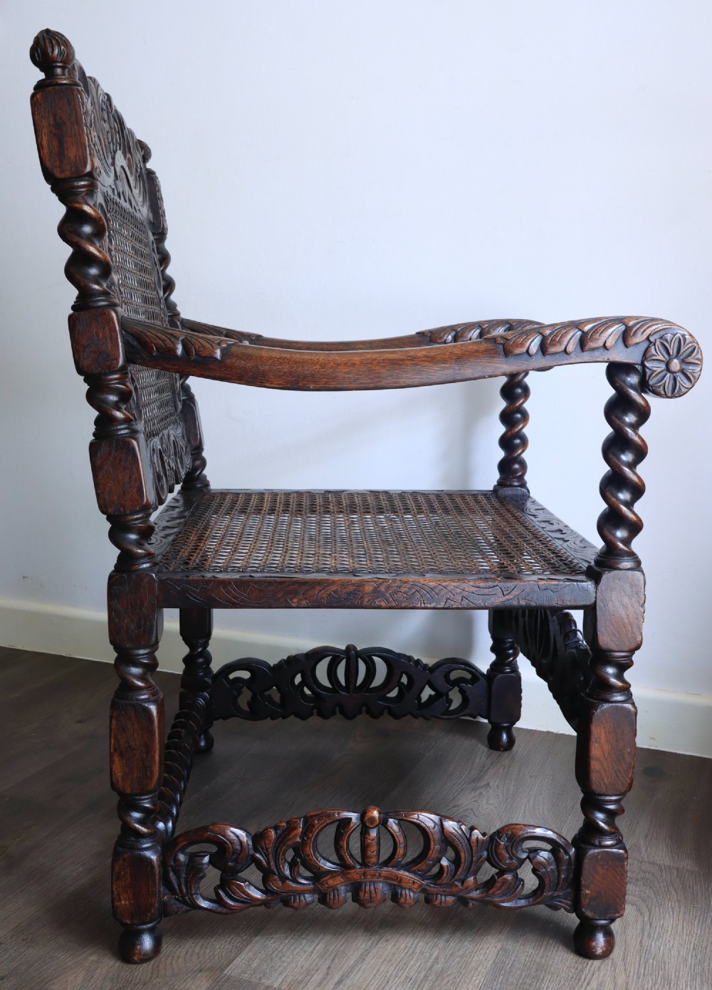 A dark carved oak armchair featuring barley twist supports, a woven cane back panel, and intricate foliate crown carving on the cresting rail. View III