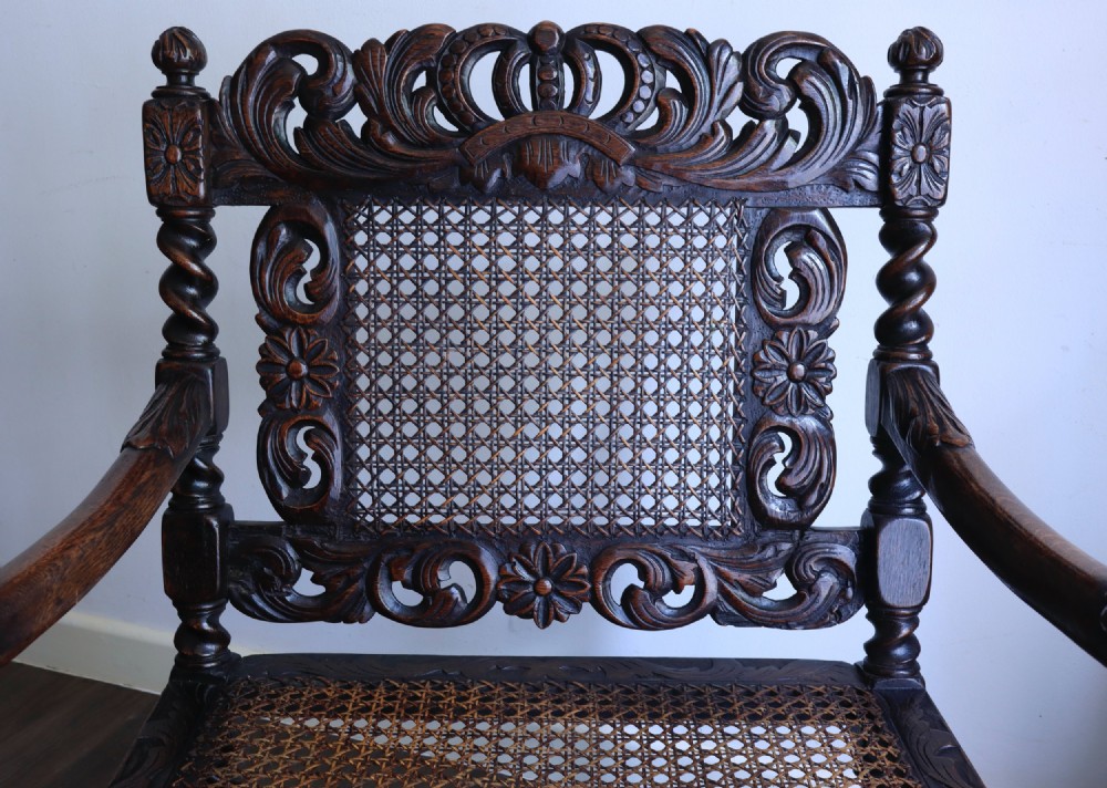 A dark carved oak armchair featuring barley twist supports, a woven cane back panel, and intricate foliate crown carving on the cresting rail. View VIII