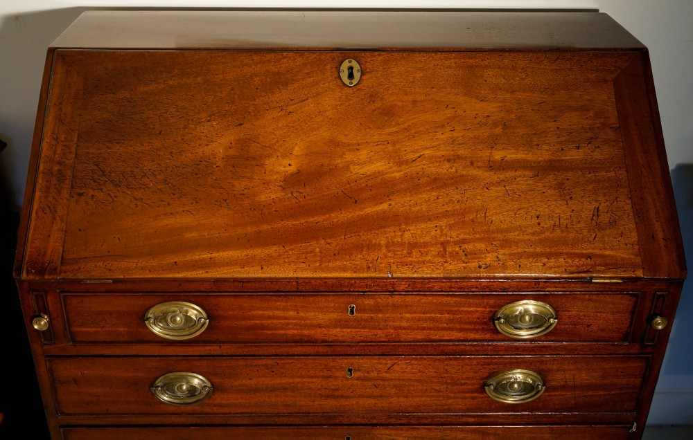 A Georgian mahogany slant-front bureau desk featuring four graduated drawers with oval brass handles on a bracket feet base. View IV