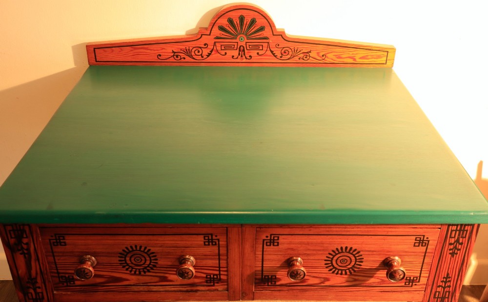 A late Victorian Aesthetic Movement pitch pine side table with a green surface, ebonised geometric incised patterns, two drawers, and turned legs with castors. View II