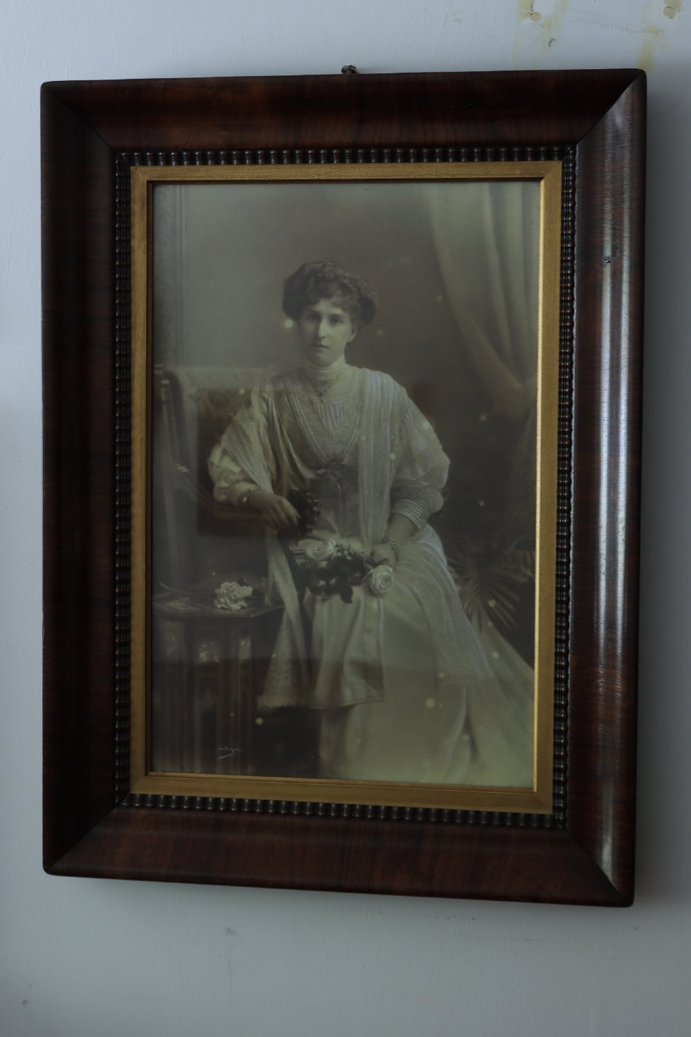 A monochrome Edwardian studio portrait photograph of a seated lady, mounted within a dark polished mahogany frame featuring a gilded inner slip.