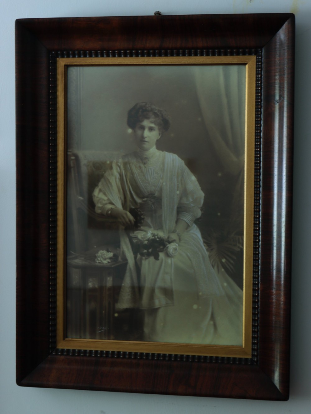 A monochrome Edwardian studio portrait photograph of a seated lady, mounted within a dark polished mahogany frame featuring a gilded inner slip. View II