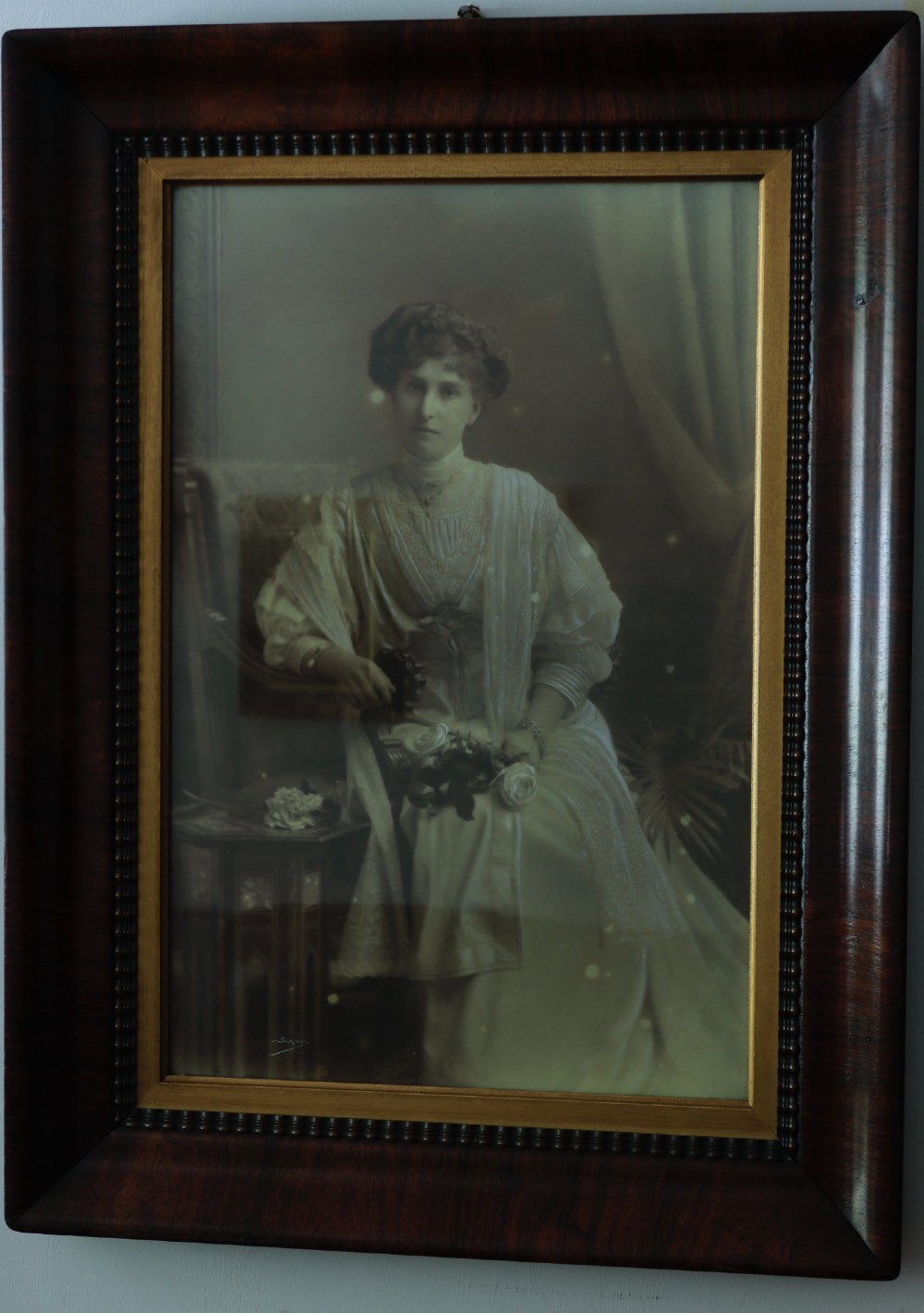 A monochrome Edwardian studio portrait photograph of a seated lady, mounted within a dark polished mahogany frame featuring a gilded inner slip. View III