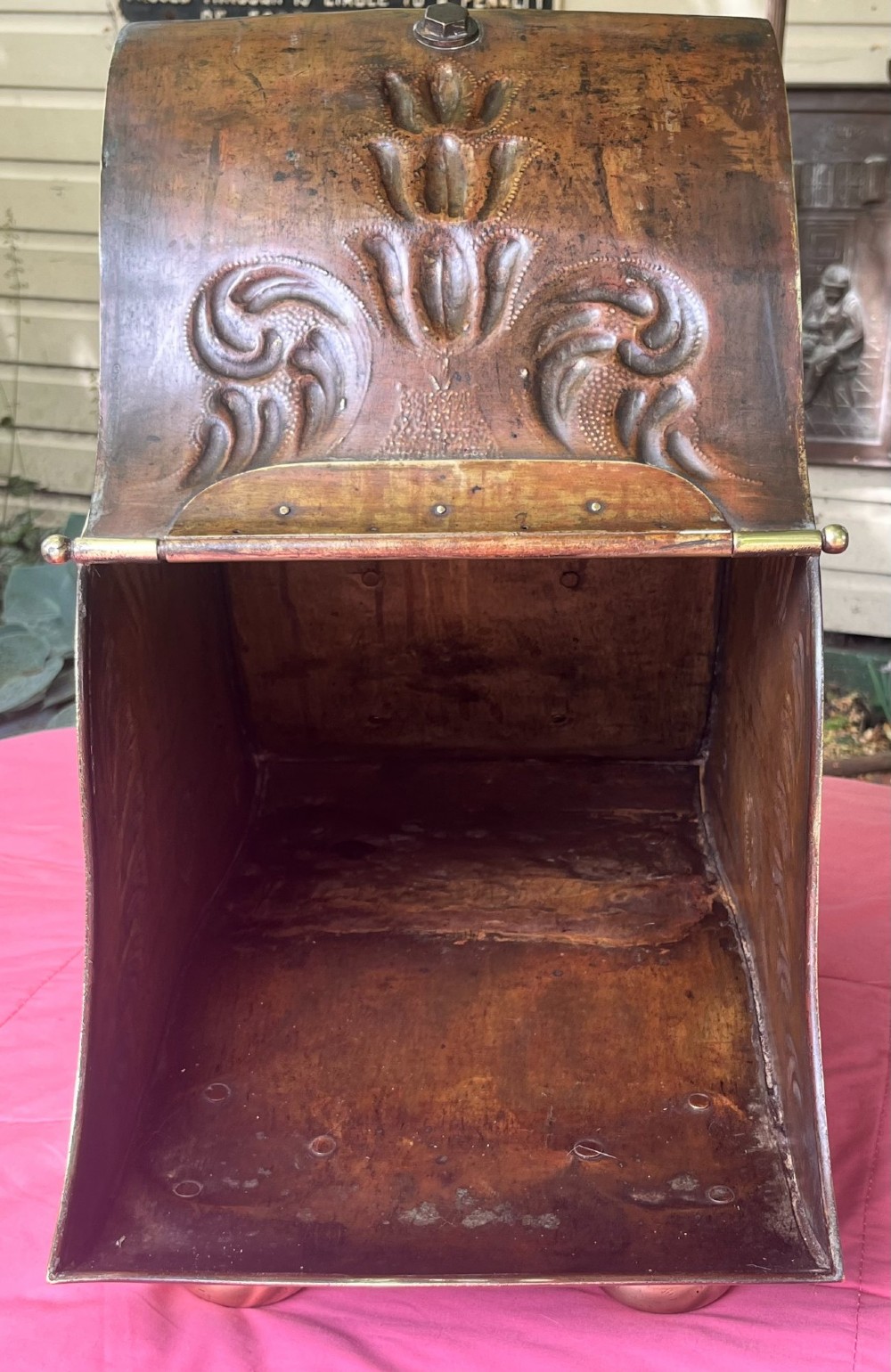 An embossed brass coal scuttle featuring a sloping hinged lid, raised foliate repousse patterns, an integrated top handle, and four raised bun feet. View IV