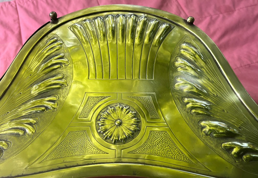 An embossed brass coal scuttle featuring a sloping hinged lid, raised foliate repousse patterns, an integrated top handle, and four raised bun feet. View VI
