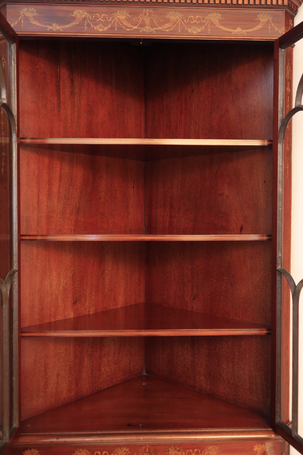 A tall mahogany standing corner cupboard featuring a broken pediment, upper glass doors with Gothic astragal glazing bars, and lower panel doors detailed with intricate marquetry inlay. View VII