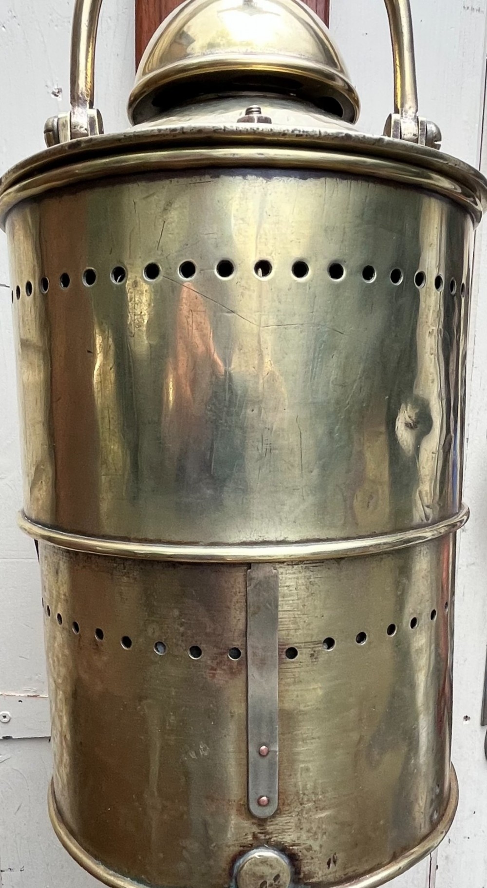 An antique brass wall lantern featuring a clear glass globe enclosed in a vented brass frame, suspended from a cast brass mascaron wall mount. View VII