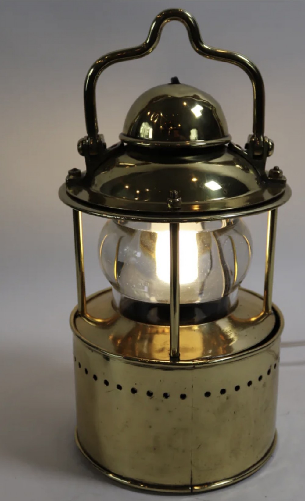 An antique brass wall lantern featuring a clear glass globe enclosed in a vented brass frame, suspended from a cast brass mascaron wall mount. View VIII