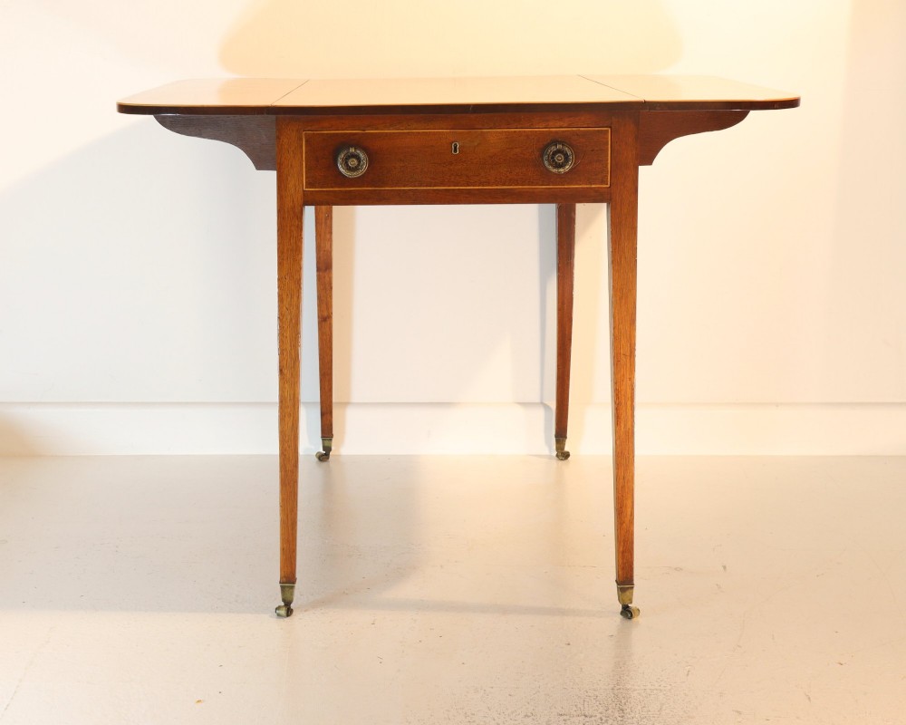 An antique mahogany Pembroke table featuring drop-leaf sides, crossbanded inlay borders, a single drawer with brass handles, and tapered square legs on brass castors. View IV