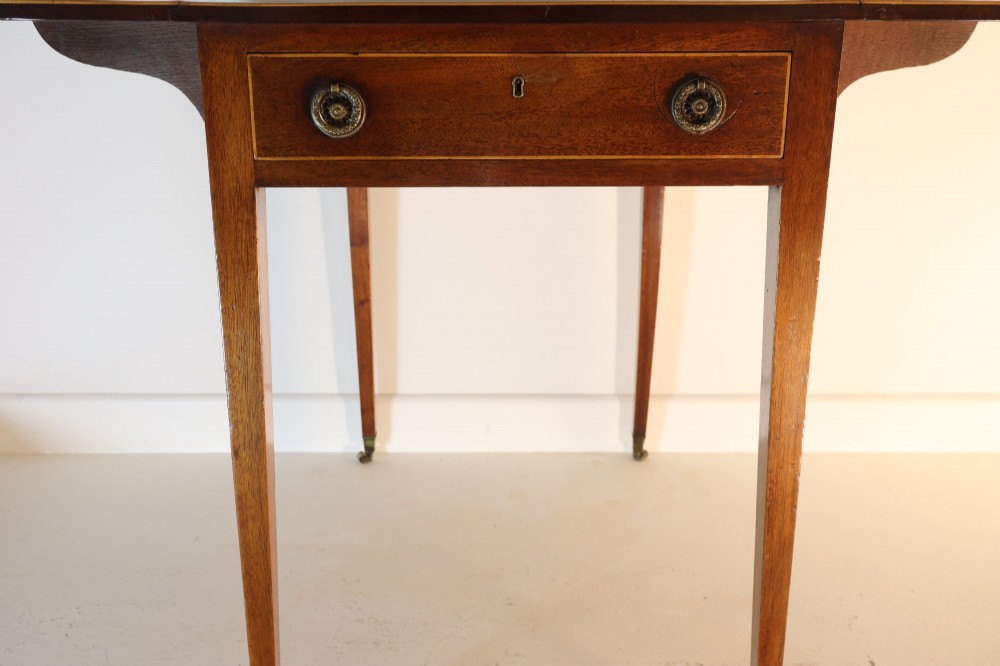 An antique mahogany Pembroke table featuring drop-leaf sides, crossbanded inlay borders, a single drawer with brass handles, and tapered square legs on brass castors. View V