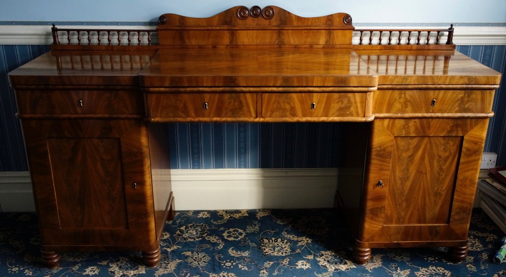 A 19th-century flame mahogany pedestal sideboard featuring a breakfront central section, twin cupboard doors, drawers, and a spindle gallery back rail with carved cresting.