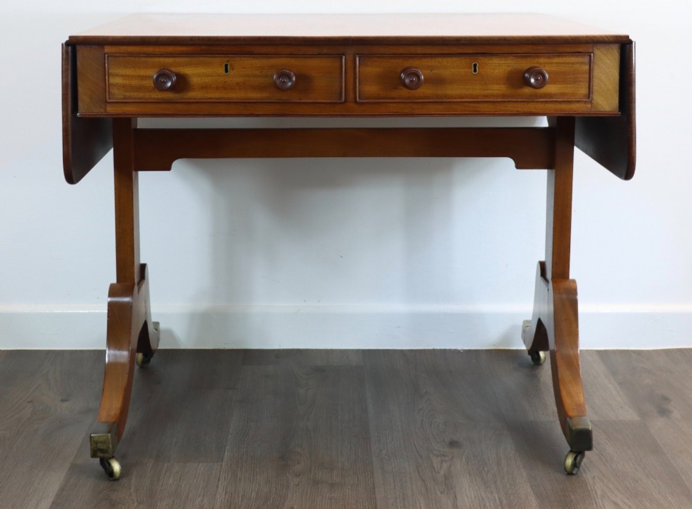 A Regency mahogany sofa table featuring two drop-leaf ends, two frieze drawers with turned wooden handles, and splayed legs with brass castors. View II