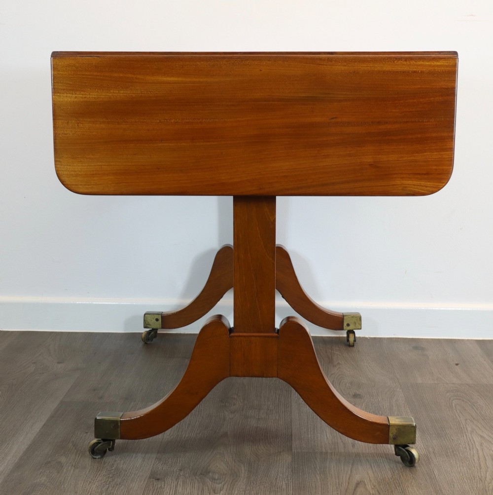 A Regency mahogany sofa table featuring two drop-leaf ends, two frieze drawers with turned wooden handles, and splayed legs with brass castors. View III