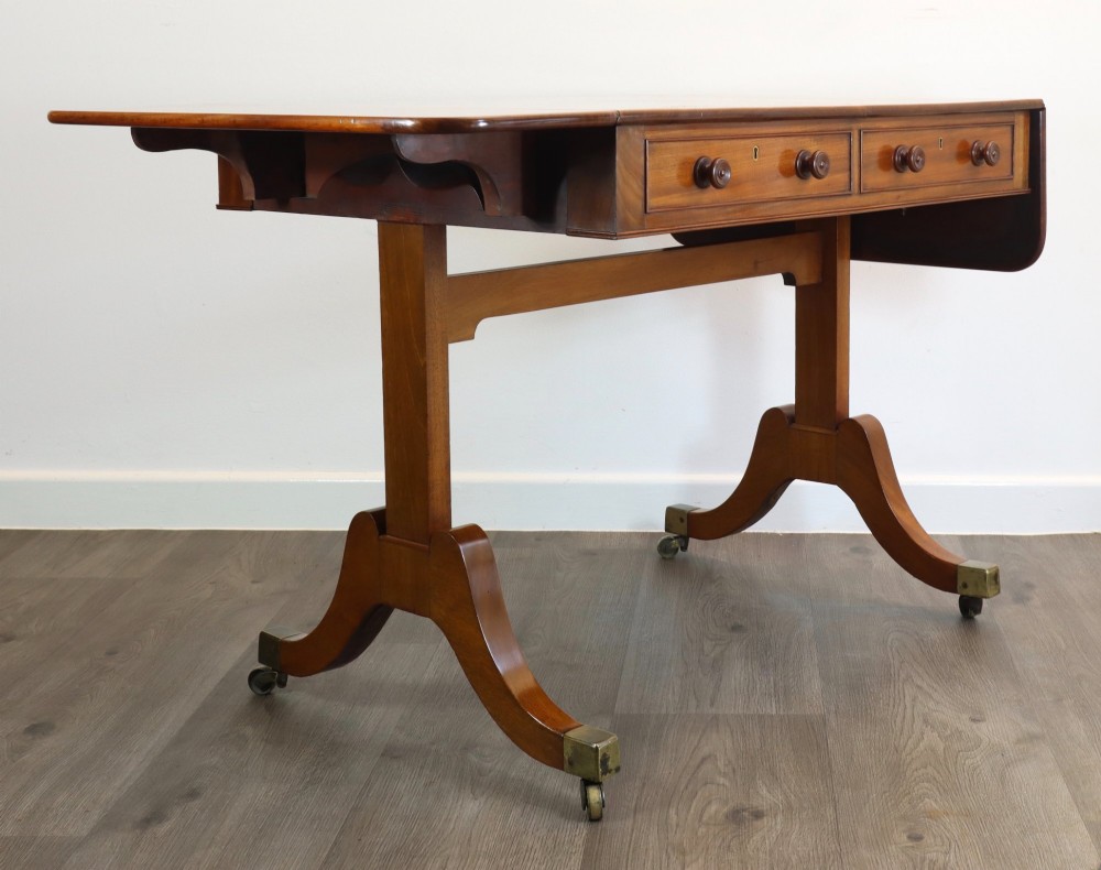 A Regency mahogany sofa table featuring two drop-leaf ends, two frieze drawers with turned wooden handles, and splayed legs with brass castors. View IV