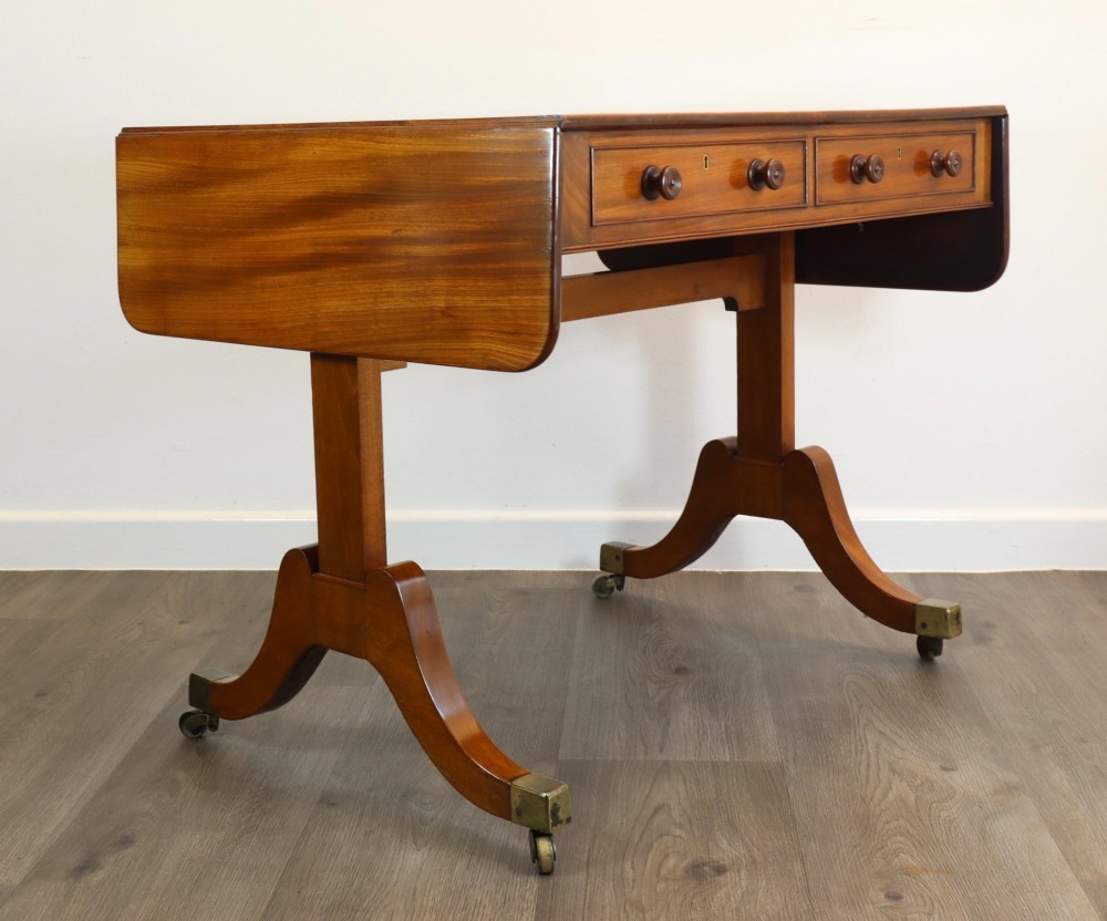 A Regency mahogany sofa table featuring two drop-leaf ends, two frieze drawers with turned wooden handles, and splayed legs with brass castors. View V