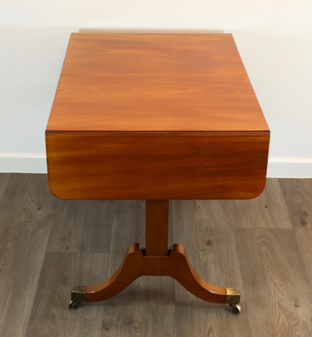 A Regency mahogany sofa table featuring two drop-leaf ends, two frieze drawers with turned wooden handles, and splayed legs with brass castors. View VI
